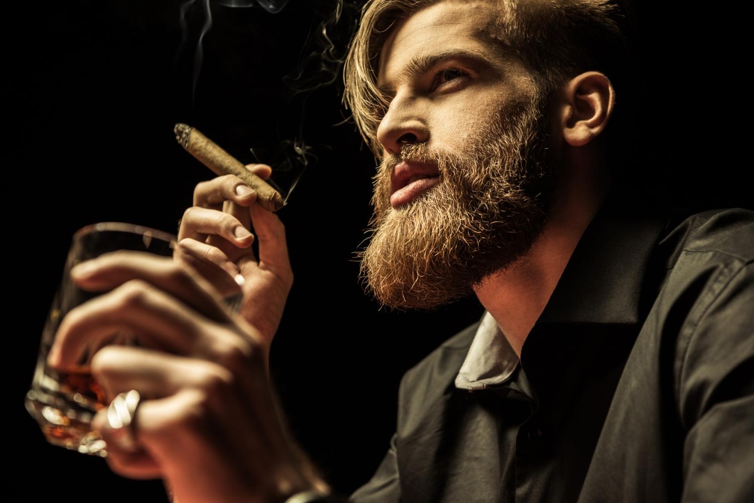 Handsome Bearded Man Holding Glass Of Whisky And Smoking Cigar On Black Stag 